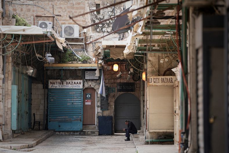 Un hombre se sienta junto a una puerta cerrada en la iglesia del Santo Sepulcro y comercios cerrados en el casco viejo de Jerusalén, que sigue vedado a los visitantes durante la guerra con Irán, el viernes 27 de marzo de 2026. (AP Foto/Mahmoud Illean)