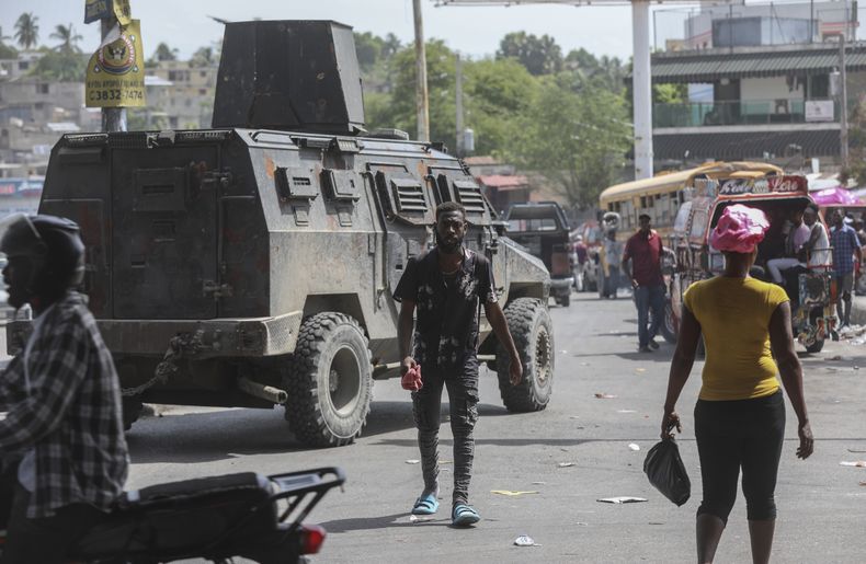 Varias personas pasan frente a un vehículo blindado de la policía que patrulla las calles de Puerto Príncipe, Haití, el lunes 15 de julio de 2024. (AP Foto/Odelyn Joseph)