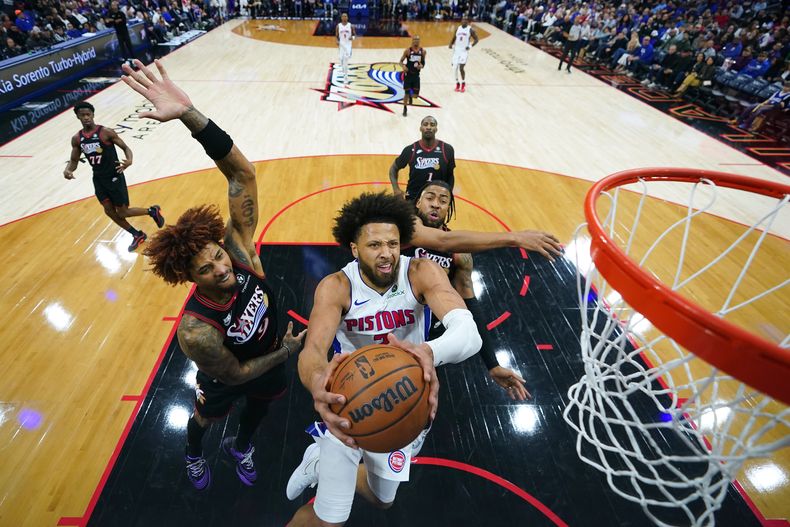 Cade Cunningham, centro, de los Pistons de Detroit, se alza para encestar ante la presión defensiva de Kelly Oubre Jr., izquierda, y Trendon Watford, de los 76ers de Filadelfia, durante la segunda mitad del juego de baloncesto de la NBA, el domingo 9 de noviembre de 2025, en Filadelfia. (AP Foto/Matt Slocum)
