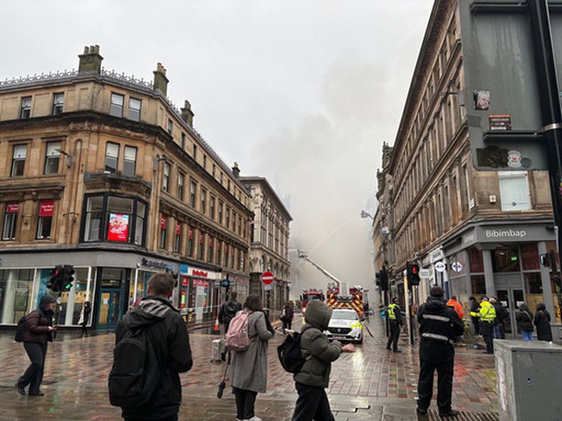 Gente mira una humareda que se eleva mientras los bomberos remojan los restos de un incendio en un edificio vecino a la estación central de Glasgow el domingo en Glasgow, Escocia, el lunes 9 de marzo de 2026. (Lucinda Cameron/PA via AP)