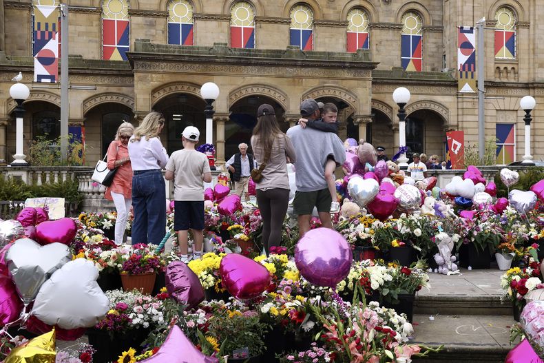 ARCHIVO – Un grupo de personas mira una ofrenda floral en el centro artístico de Atkinson en Southport, Inglaterra, el lunes 5 de agosto de 2024 después de que tres niñas fueran asesinadas en un ataque con arma blanca en un club vacacional con temática de Taylor Swift una semana antes. (AP Foto/Darren Staples, Archivo)
