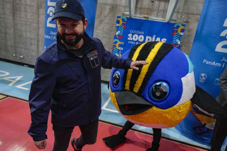 El presidente de Chile Gabriel Boric camina junto a la mascota de los Juegos Panamericanos Fiu, a la llegada al evento que marca los 100 días para el inicio de la justa en el centro deportivo La Pintana en Santiago, Chile el miércoles 12 de julio del 2023. (AP Foto/Esteban Felix)