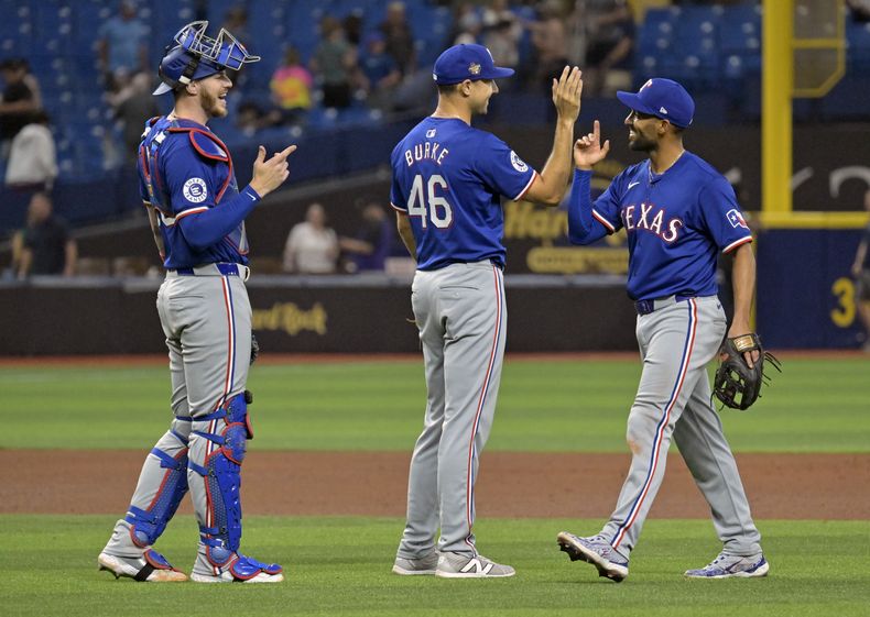 El receptor de los Rangers de Texas Jonah Heim, a la izquierda, el relevista Brock Burke (46) y Marcus Semien celebran una victoria sobre los Rays de Tampa Bay en un juego de béisbol el lunes 1 de abril de 2024 en St. Petersburg, Florida (AP Foto/Steve Nesius)