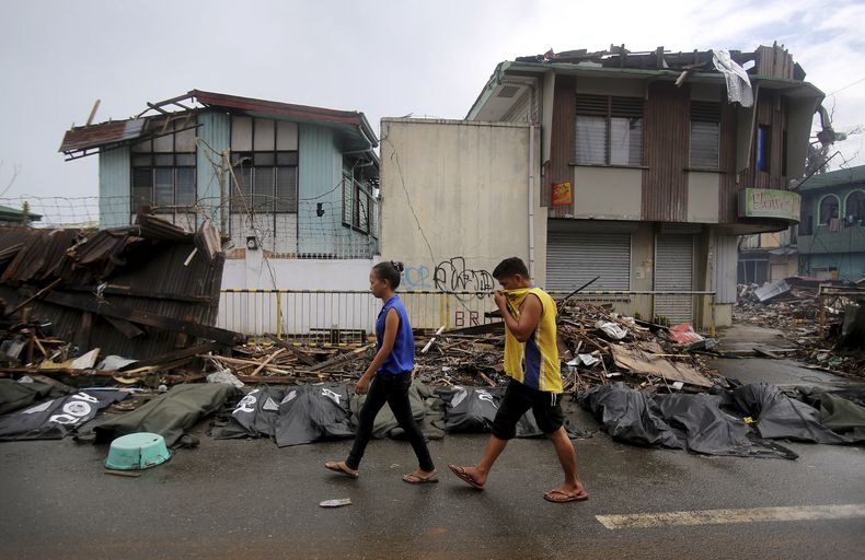 Dos personas pasan junto a cad&aacute;veres de las v&iacute;ctimas del tif&oacute;n Haiyan, el s&aacute;bado 16 de noviembre del 2013, en la ciudad de Taclob&aacute;n, en el centro de las Filipinas. (Foto AP/Wong Maye-E)