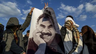 Dos jóvenes muestran un cartel con la imagen de Abdullah Ocalan, el encarcelado líder del Partido de los Trabajadores del Kurdistán, o PKK, mientras se reúnen para seguir por televisión como una delegación del Partido Popular por la Igualdad y la Democracia hacen pública una declaración de Ocalan, en Diyarbakir, Turquía, el 27 de febrero de 2025. (AP Foto/Metin Yoksu)