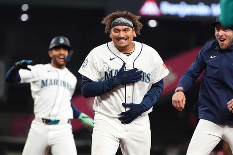 Josh Naylor, centro, de los Marineros de Seattle, celebra con Julio Rodríguez, izquierda, y Luke Raley, derecha, después de batear el sencillo que dejó tendidos a los Atléticos durante la novena entrada del juego de béisboil de Grandes Ligas el miércoles 22 de abril de 2026, en Seattle. (AP Foto/Lindsey Wasson)