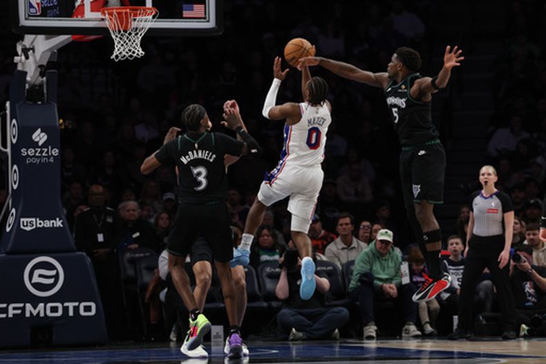 El guardia de los 76ers de Filadelfia, Tyrese Maxey (0), sube para lanzar ante el guardia de los Timberwolves de Minnesota, Anthony Edwards (5), durante la primera mitad de un juego de baloncesto de la NBA, el domingo 22 de febrero de 2026, en Minneapolis. (Foto AP/Stacy Bengs)