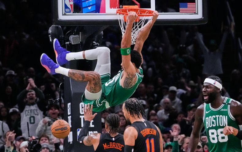 Jayson Tatum, de los Celtics de Boston, cuelga del aro tras realizar una clavada ante los Knicks de Nueva York en el duelo del viernes 23 de octubre de 2026 (AP Foto/Charles Krupa)
