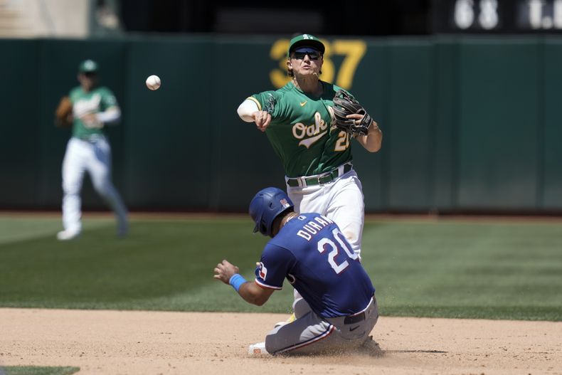 El segunda Zack Gelof, atrás, de los Atléticos de Oakland, lanza a primera después de forzar en segunda a Ezequiel Duran (20), de los Rangers de Texas, durante la octava entrada del juego de béisbol, el miércoles 9 de agosto de 2023, en Oakland, California. Marcus Semien llegó a salvo a primera en la jugada. (AP Foto/Godofredo A. Vásquez)