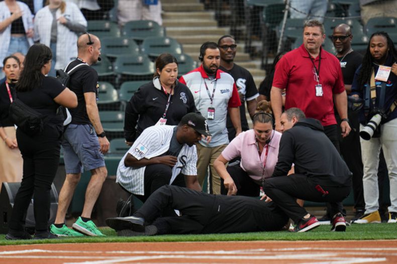 Varias personas atienden a un hombre que se desplomó mientras cantaba Life Every Voice and Sing antes de un partido de béisbol entre los Rays de Tampa Bay y Medias Blancas de Chicago, el miércoles 15 de abril de 2026, en Chicago. (Foto AP/Erin Hooley)