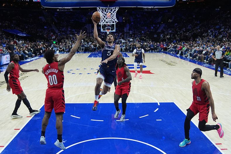 Quentin Grimes, de los 76ers de Filadelfia, se alza para encestar frente a Jrue Holiday, de los Trail Blazers de Portland, durante la primera mitad del juego de baloncesto de la NBA, el domingo 15 de marzo de 2026, en Filadelfia. (AP Foto/Matt Rourke)