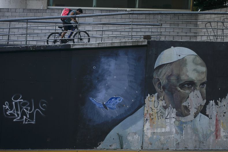 ARCHIVO - Un hombre monta en bicicleta cerca de un mural desgastado del papa Francisco en Buenos Aires, Argentina, el 2 de marzo de 2023. (AP Foto/Natacha Pisarenko, Archivo)