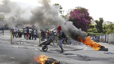Un hombre empuja una carretilla frente a neumáticos en llamas durante una protesta para exigir la renuncia del primer ministro Ariel Henry, el jueves 7 de marzo de 2024, en Puerto Príncipe, Haití. (AP Foto/Odelyn Joseph)