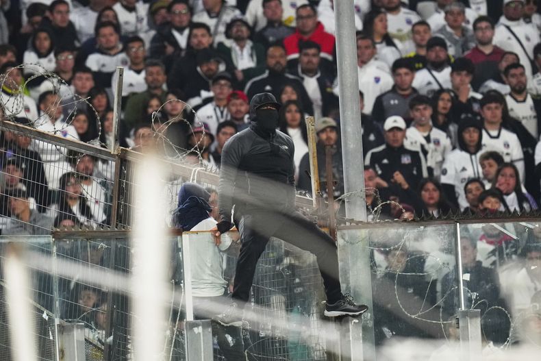 Un hincha trepa en un panel de cristal durante un partido de la Copa Libertadores entre Colo Colo de Chile y Fortaleza de Brasil en Santiago, el jueves 10 de abril de 2025 (AP Foto/Esteban Félix)