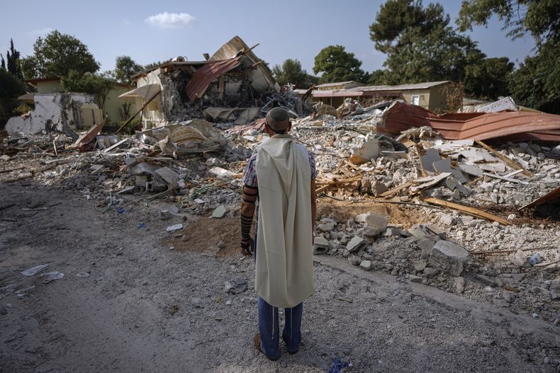 Un hombre israelí, con un chal de rezo, ora junto a viviendas destruidas por insurgentes de Hamás en el kibutz de Beeri, Israel, el 22 de octubre de 2023. El kibutz fue asaltado por insurgentes de Hamás desde la cercana Gaza el 7 de octubre, cuando mataron y capturaron a muchos israelíes. (AP Foto/Ariel Schalit)