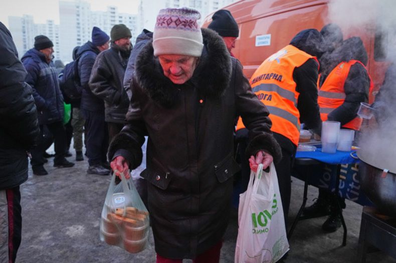 Una anciana carga bolsas en un punto de distribución de alimentos calientes durante un apagón causado por los repetidos ataques aéreos rusos a la red eléctrica del país, en Kiev, Ucrania, el lunes 2 de febrero de 2026. (Foto AP/Sergey Grits)