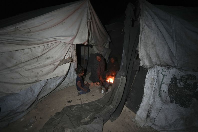 Shireen Daifallah, que fue desplazada con sus hijos del norte de Gaza, revisa el fuego junto a su tienda de campaña en un campamento de desplazados en Deir al-Balah, Franja de Gaza, el sábado 30 de noviembre de 2024. (Foto AP/Abdel Kareem Hana)