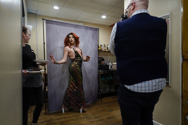 Una mesera hace una pausa con platos mientras la drag queen Harpy Daniels, alias Joshua Kelley, posa para una fotografía tomada por Ryan Geiger, derecha, antes del espectáculo Daniels Family Values en Heritage Restaurant en Shamokin, Pennsylvania, el 16 de abril de 2022. Suboficial de primera clase de la Marina de Estados Unidos, Kelley nombrado embajador digital por la Armada de Estados Unidos para tener contacto con la comunidad LGBTQ+. (Foto AP/Carolyn Kaster)