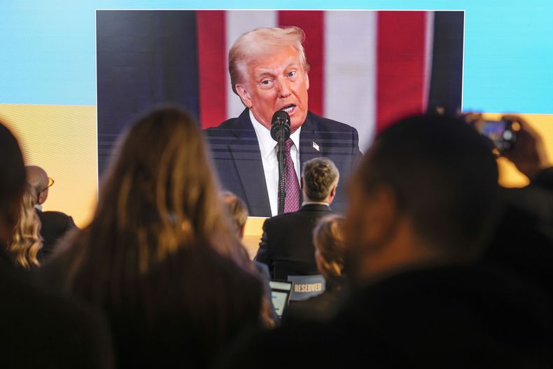 Varias personas siguen la toma de posesión de Donald Trump en pantallas en la casa de Ucrania, en el Foro Económico Mundial, en Davos, Suiza, el 20 de enero de 2025. (AP Foto/Markus Schreiber)