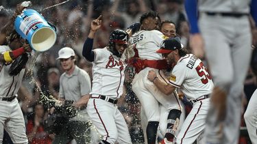 Ozzie Albies (centro) es felicitado por sus compañeros tras empujar la carrera del triunfo sobre los Dodgers de Los Ángeles, el miércoles 24 de mayo de 2023 (AP Foto/John Bazemore)
