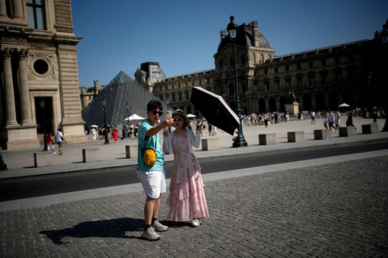 Turistas con un paraguas se toman una foto en París el lunes 22 de junio de 2026, en medio de una intensa ola de calor en Francia. (AP Foto/Christophe Ena)