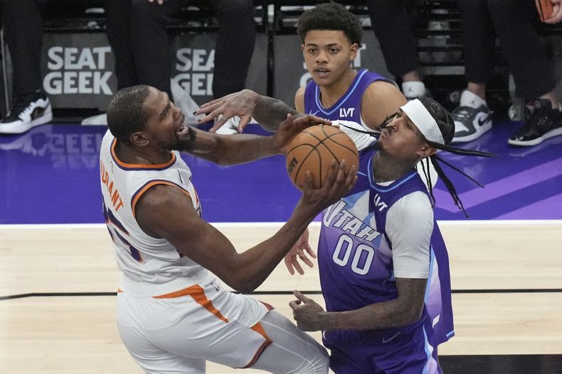 Jordan Clarkson (00), del Jazz de Utah, comete una falta a Kevin Durant, de los Suns de Phoenix, izquierda, quien llevaba el balón hacia la canasta durante la segunda mitad del juego de baloncesto de la NBA, el viernes 13 de diciembre de 2024, en Salt Lake City. (AP Foto/Rick Bowmer)