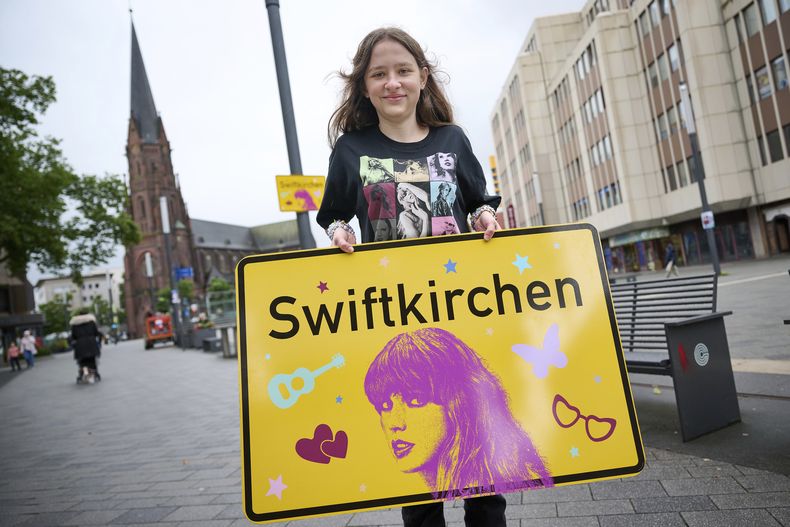 La estudiante Aleshanee Westhoff muestra un cartel de la ciudad Swiftkirchen en honor a Taylor Swift en Gelsenkirchen, Alemania, el martes 2 de julio de 2024. Los swifties están a punto de apoderarse de la ciudad alemana de Gelsenkirchen, donde la superestrella estadounidense Taylor Swift dará tres conciertos de su Eras Tour a finales de este mes. En honor al cantante, la ciudad se rebautizó como Swiftkirchen temporalmente para dar la bienvenida a las decenas de miles de fans. (Bernd Thissen/dpa via AP)