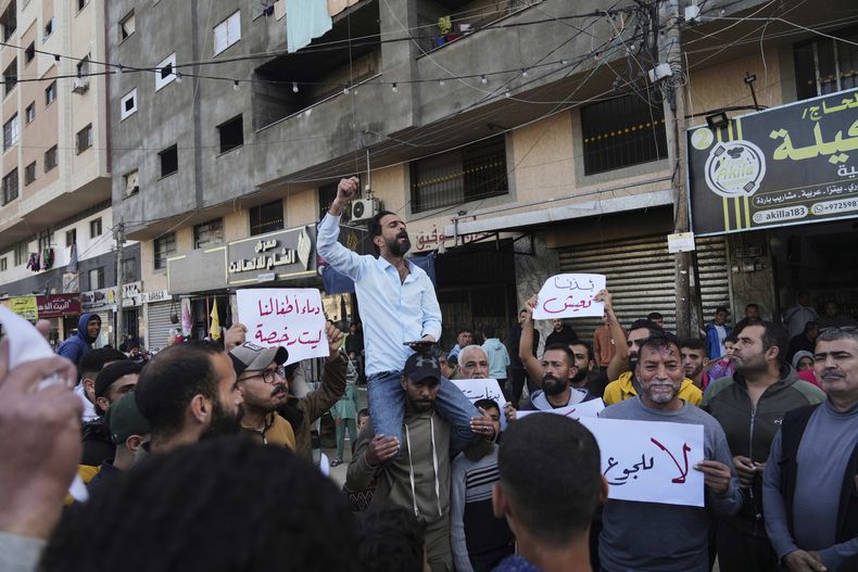 Un grupo de palestinos sostiene letreros contra la guerra mientras un hombre corea consignas de apoyo a los habitantes de Bait Lahiya que se manifestaron el martes contra Hamás, en una muestra infrecuente contra el grupo armado que gobierna el territorio, en Deir al-Balah, Franja de Gaza, el miércoles 26 de marzo de 2025. (AP Foto/Abdel Kareem Hana)