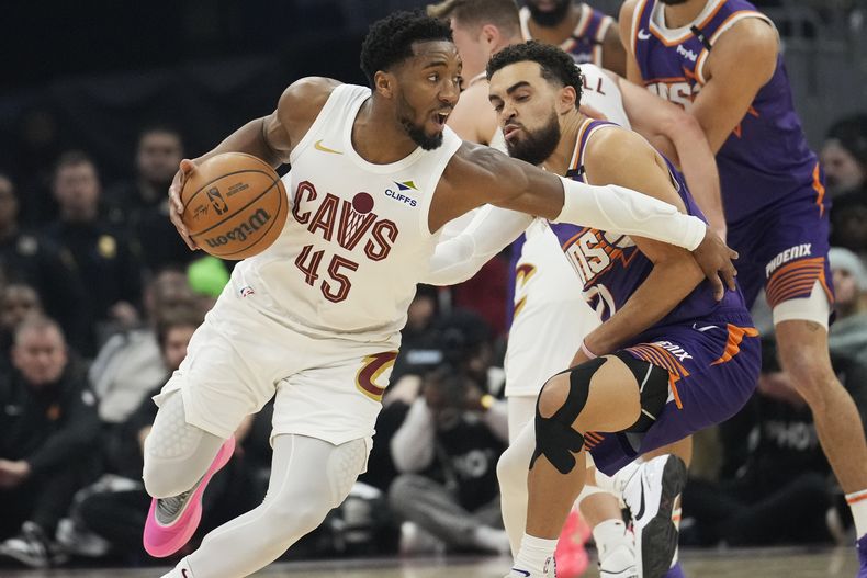 El escolta de los Cavaliers de Cleveland, Donovan Mitchell (45), conduce alrededor del escolta de los Suns de Phoenix, Tyus Jones, al frente a la derecha, en la primera mitad de un partido de baloncesto de la NBA, el lunes 20 de enero de 2025, en Cleveland. (AP Foto/Sue Ogrocki)