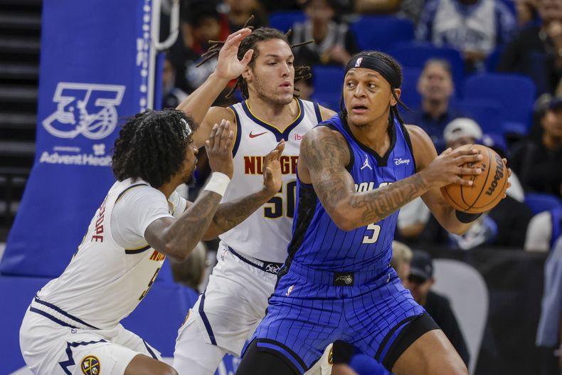 Paolo Banchero, alero del Magic de Orlando, controla el balón, marcado por Kentavious Caldwell-Pope (izquierda) y Aaron Gordon, de los Nuggets de Denver, el miércoles 22 de noviembre de 2023 (AP Foto/Kevin Kolczynski)
