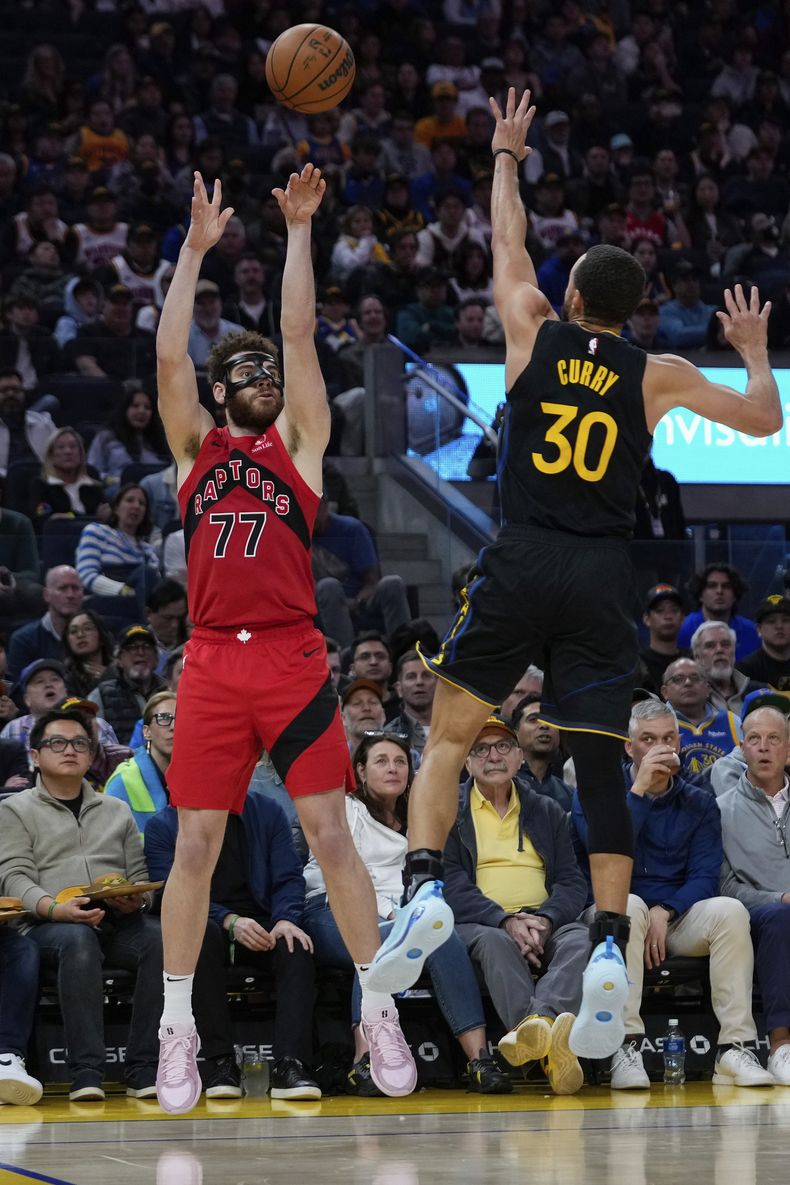El alero de los Raptors de Toronto, Jamison Battle (77), lanza una canasta de 3 puntos sobre el escolta de los Warriors de Golden State, Stephen Curry (30), durante la segunda mitad de un partido de baloncesto de la NBA, el jueves 20 de marzo de 2025, en San Francisco. (AP Foto/Godofredo A. Vásquez)