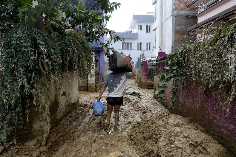 Un hombre camina en un callejón enlodado, cargando pertenencias rescatadas de su casa en Katmandú, Nepal, el lunes 30 de septiembre de 2024, tras una inundación provocada por las fuertes lluvias. (AP Foto/Gopen Rai)