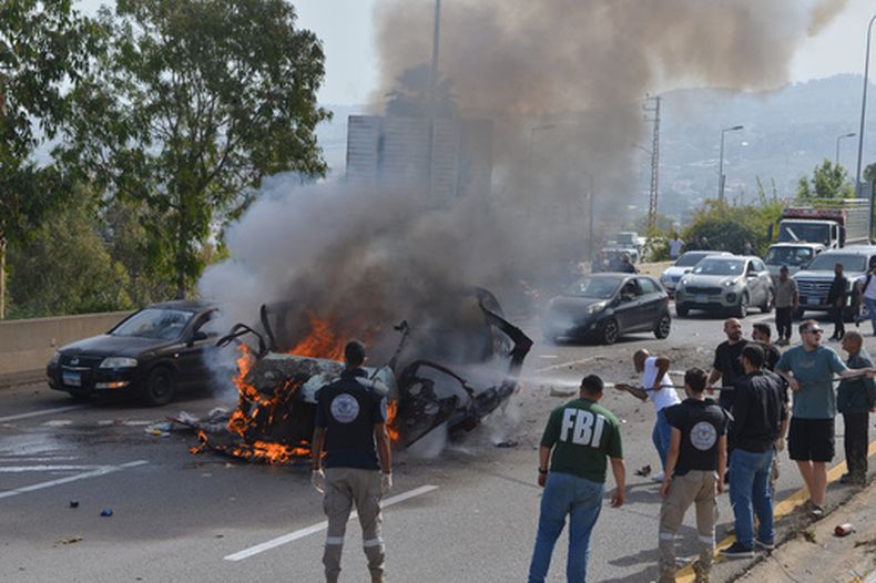 Fuerzas de seguridad y personal de emergencia se congregan alrededor de un vehículo en llamas debido a un ataque aéreo israelí, mientras un hombre intenta apagar el fuego, el miércoles 13 de mayo de 2026, en la ciudad costera de Jiyeh, al sur de Beirut, Líbano. (AP Foto/Mustafa Jamalddine)