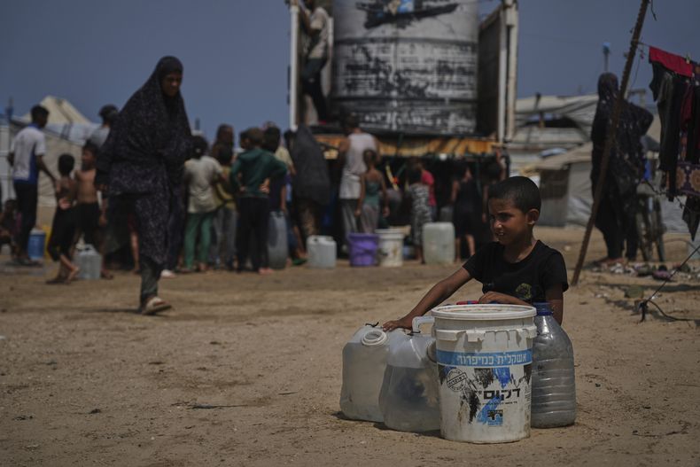 Palestinos desplazados se reúnen para recoger agua de un camión durante una ola de calor en un campamento improvisado en Jan Yunis, en la Franja de Gaza, el miércoles 13 de agosto de 2025. (AP Foto/Abdel Kareem Hana)