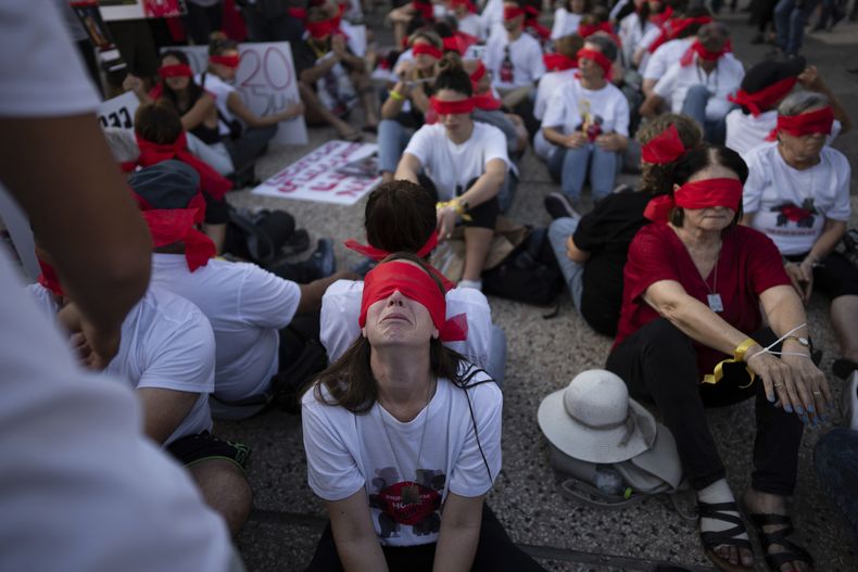 Residentes del kibbutz de Kfar Azza se cubren los ojos y se atan las manos durante una manifestación en solidaridad con sus amigos y familiares retenidos en la Franja de Gaza, en Tel Aviv, Israel, el 2 de noviembre de 2023. Insurgentes de Hamás asaltaron la pequeña comunidad agrícola durante su sangriento ataque transfronterizo desde la Franja el 7 de octubre. Dieciocho residentes fueron secuestrados y llevados al enclave palestino, incluyendo siete menores, el más pequeño de apenas tres años. (AP Foto/Oded Balilty)