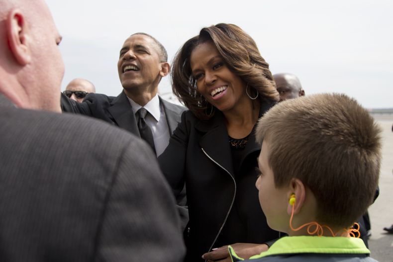 El presidente Barack Obama y la primera dama Michelle Obama saludan a un grupo de personas tras descender del avi&oacute;n presidencial en la pista del Aeropuerto Internacional John F. Kennedy en Nueva York, el viernes 11 de abril de 2014, al viajar a la