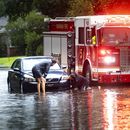Dos personas atan un cabo a un auto varado en una calle anegada debido a las fuertes lluvias de la tormenta tropical Debby, el 5 de agosto de 2024, en Savannah, Georgia. (AP Foto/Stephen B. Morton)