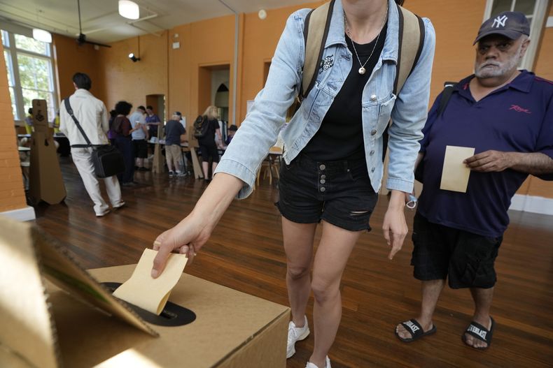 Un hombre, a la derecha, espera mientras una mujer vota en un centro de votación en Redfern en las últimas horas de votación en el primer referendo en Australia en una generación, para decidir si se consagraba en la constitución una institución indígena que aborde la situación desfavorecida de la comunidad indígena australiana. (AP Foto/Rick Rycroft)
