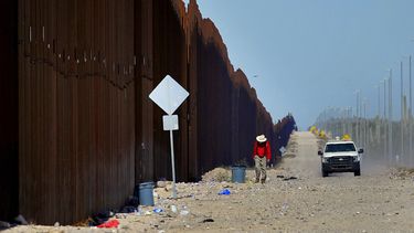 ARCHIVO - El maestro jubilado Tom Wingo, de Samaritanos Sin Fronteras, recoge basura a lo largo de la valla fronteriza mientras pasa un vehículo de las autoridades de aduanas el 29 de agosto de 2023 en el Parque Nacional de Cactus Órgano cerca de Lukeville, Arizona. (AP Foto/Matt York, Archivo)