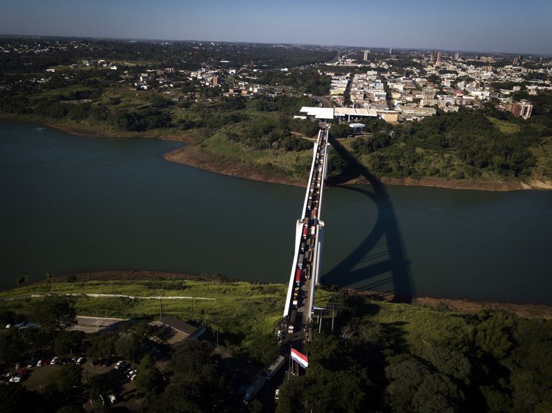 ARCHIVO - Varios camiones hacen fila el 23 de junio de 2020 en el Puente Internacional de la Amistad sobre el río Paraná, la frontera entre Foz do Iguazu, Brasil, arriba, y Ciudad del Este, Paraguay. (AP Foto/Jorge Saenz, archivo)