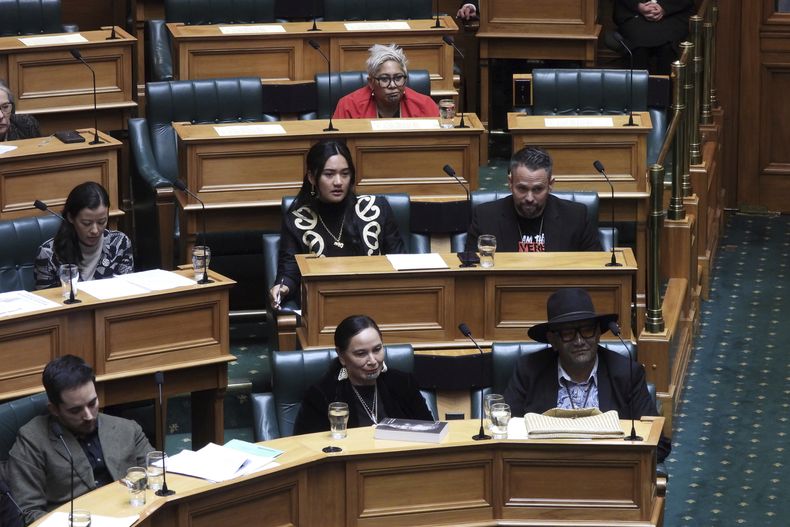 Los legisladores neozelandeses Hana-Rāwhiti Maipi-Clarke (centro, 2da fila), Debbie Ngarewa-Packer (centro, 1ra fila) y Rawiri Waititi (abajo, derecha), que fueron suspendidos por protestar realizando una haka en noviembre, observan mientras otros parlamentarios debaten sobre sus sanciones, en Wellington, Nueva Zelanda, el 5 de junio de 2025. (AP Foto/Charlotte Graham-McLay)