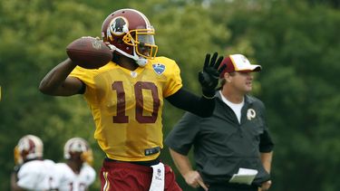americateve | El jugador de los Redskins de Washington, Robert Griffin III, izquierda, lanza un pase en un entrenamiento el 27 de julio de 2014 en Roanoke, Virginia. (AP Photo/Alex Brandon, File)