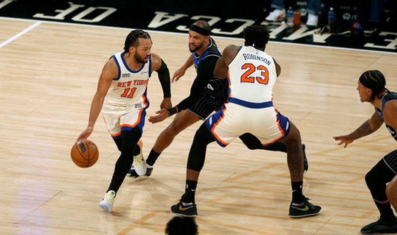 El base de los Knicks de Nueva York Jalen Brunson avanza con el balón frente a Jalen Suggs del Magic y su compañero Mitchell Robinson en el encuentro del domingo 7 de diciembre del 2025. (AP Foto/John Munson)