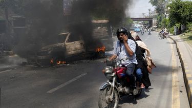 Una moto con varias personas a bordo circula junto a una camioneta incendiada por partidarios del ex primer ministro paquistaní Imran Khan, en Lahore, Pakistán, el 11 de mayo de 2023. (AP Foto/K.M. Chaudary)