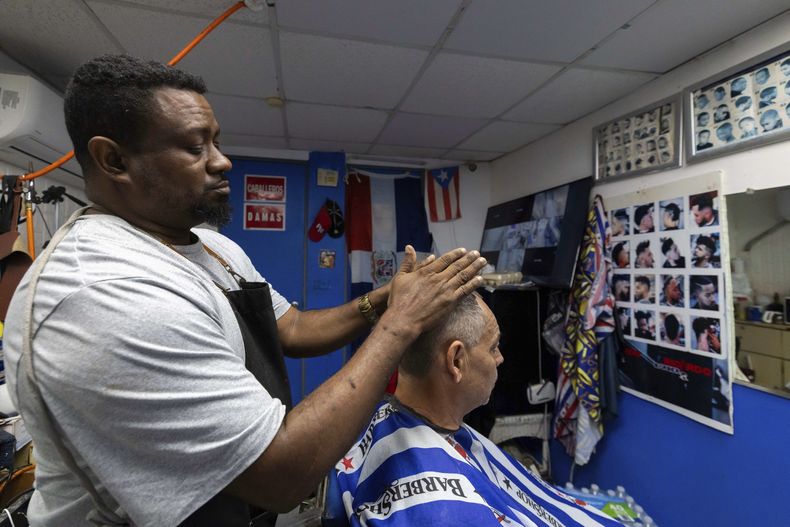 Ricardo Perez, un barbero dominicano que ha vivido en Puerto Rico más de 20 años, explica cómo su negocio ha perdido clientela desde que comenzaron las redadas entre comunidades inmigrantes durante el segundo gobierno de Trump, mientras corta el pelo en San Juan, Puerto Rico, el viernes 14 de marzo de 2025. (AP Foto/Alejandro Granadillo)