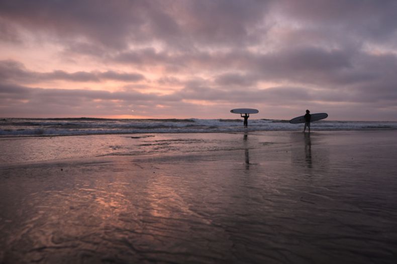 Surfistas entran en el océano Pacífico al atardecer, el jueves 1 de octubre de 2026 en Encinitas, California. (AP Foto/Gregory Bull)