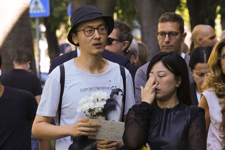 Un hombre que lleva flores y una nota dirigida en italiano y mandarín a la familia del Signor Giorgio Armani espera en la fila para presentar sus respetos al diseñador de moda Giorgio Armani, quien yace en el Armani/Teatro en Milán, norte de Italia, el sábado 6 de septiembre de 2025. (Foto AP/Antonio Calanni)