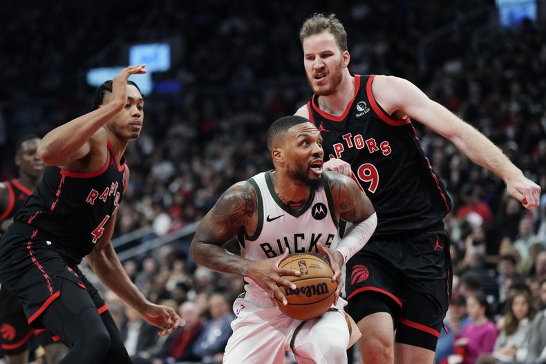 Damian Lillard, de los Bucks de Milwaukee, avanza entre Scottie Barnes (izquierda) y Jakob Poeltl, de los Raptors de Toronto, en el encuentro del miércoles 15 de noviembre de 2023 (Frank Gunn/The Canadian Press via AP)