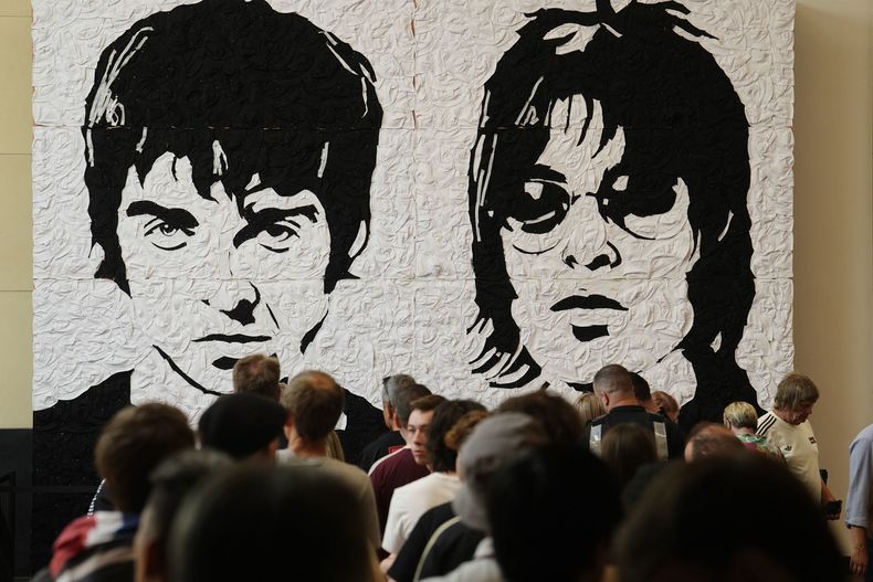Fans de Oasis se toman fotos frente al Wonder Wall, un mural del artista galés Nathan Wyburn hecho con 3.000 sombreros de pescador blancos y negros que representan a Liam y Noel Gallagher, en el centro comercial St Davids en Cardiff, antes del primer espectáculo de su tan esperada gira de reunión que comienza en Gales, el viernes 4 de julio de 2025. (Jordan Pettitt/PA via AP)