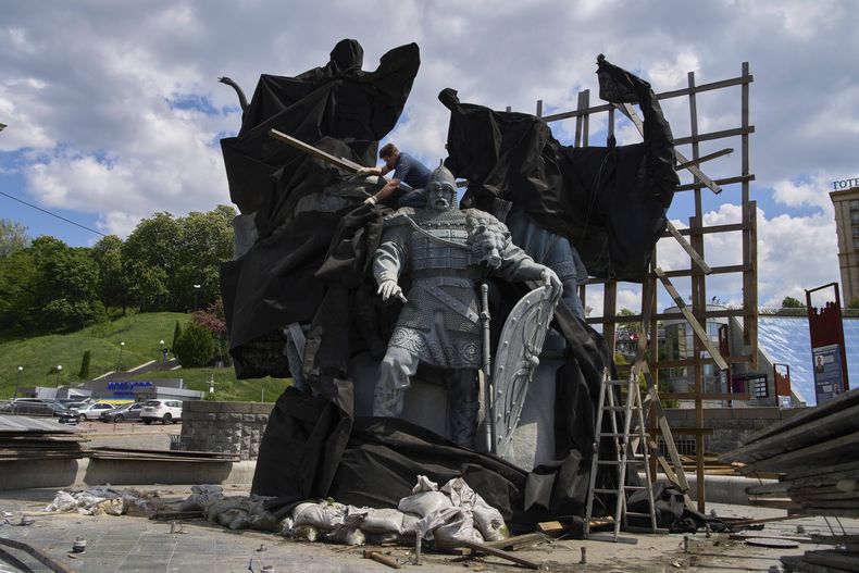 Trabajadores municipales retiran la cobertura que protegía un monumento a los fundadores legendarios de Kiev de ataques de misiles rusos en el cuarto año de la guerra entre Rusia y Ucrania, en la plaza principal de Kiev, Ucrania, el miércoles 21 de mayo de 2025. (AP Foto/Efrem Lukatsky)